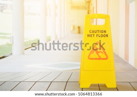 Sign showing warning of caution wet floor with walkway blur background and sunlight in summer time at high school or university. Selective focus and filtered process.
