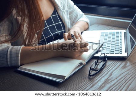 Business women write down on notebook and have laptop and pen and glass on the wood table have light ray from sunlight.
