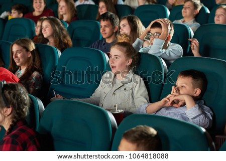 Sideview of laughing children watching movie in the cinema hall. Kids look funny, happy and satisfied. Boys and girls wearing colorful clothes with different prints and smiling.