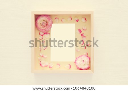 Image of delicate pastel pink beautiful flowers arrangement and empty vintage photo frame over white wooden background. Flat lay, top view. For photography mockup montage