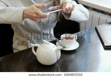 Unrecognizable woman's hands pictures of teapot and Cup in a cafe on her cell phone. Side view.