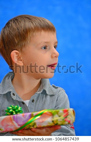 A boy with a gift in his hands in the studio with an open mouth on a blue background looking out into the distance