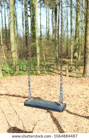 Emtpy black swing in forest surrounded. Sunny day in spring.