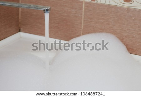 Water flows in a bubble bath. A lot of white foam. Closeup.