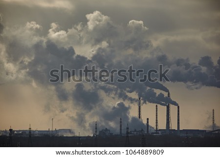 The plant emits smoke and smog from the pipes at mist cloudy, pollutants enter the atmosphere. Environmental disaster. Harmful emissions into. Exhaust gases. Chemical industry against the sky. Royalty-Free Stock Photo #1064889809