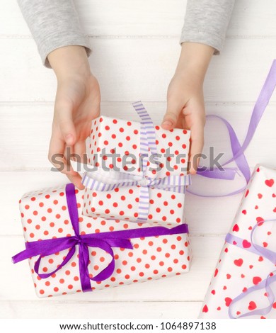 Little kid's hands holding gift box wrapped in heart patterned wrapping paper and bound with a neat purple bow and ribbon, top view