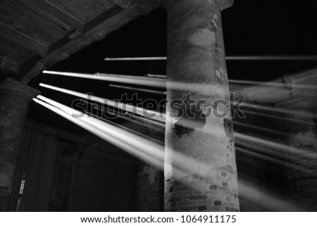 Column wrapped in beams of light coming down from holes in the ceiling. Black and white Royalty-Free Stock Photo #1064911175