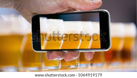 Hand taking picture of beer glasses through smart phone at bar