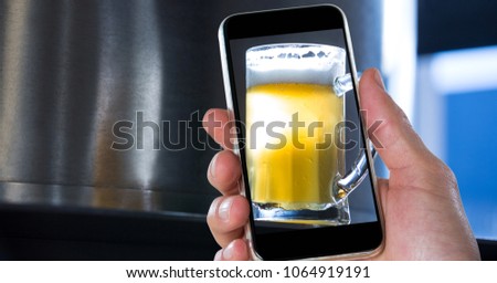 Hand taking picture of beer glass through smart phone at bar