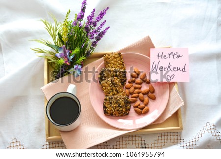 Healthy breakfast with almonds and granola bars  and a cup of coffee on a wooden tray with Hello Weekend text on a note  Royalty-Free Stock Photo #1064955794