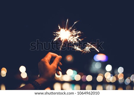 Motion Blurred Sparklers in blur woman hand holding at night city with bokeh reflect on river side, vintage film grain style.Abstract blur sparklers for celebration christmas,festival party background