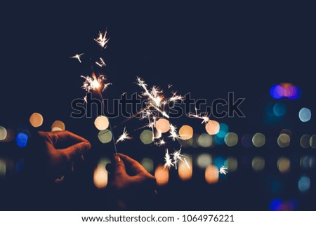 Abstract Blurred Sparklers in blur woman hand holding at night city with bokeh reflect on river side, Vintage Film grain style. blur sparklers for celebration christmas party festival background.