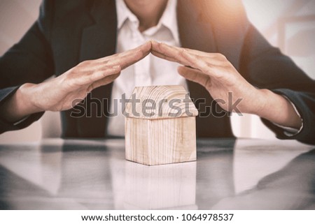 Composite image of insurer protecting a house by his hands