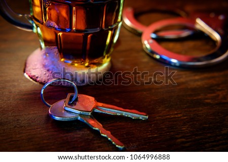 Mug of frothy beer with handcuffs and keys symbolizing drunk driving arrest Royalty-Free Stock Photo #1064996888