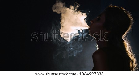 Beautiful young woman profile in backlight smoking hookah with a lot of smoke isolated black background. Club party menu concept