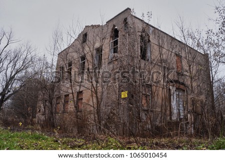 Old house falling apart and abandoned surrounded by leafless trees and bushes. Sign saying no entry.