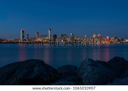 Panoramic view of the Liverpool skyline across the Mersey river at night, with pink and turquoise reflections in the water, as seen from the Seacombe, just across the river Royalty-Free Stock Photo #1065010907