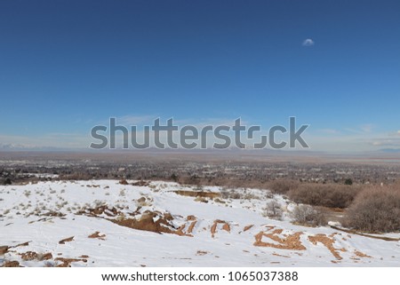 Snow covered red dirt above Bountiful city Utah, with blue sky and mountains in the distance
