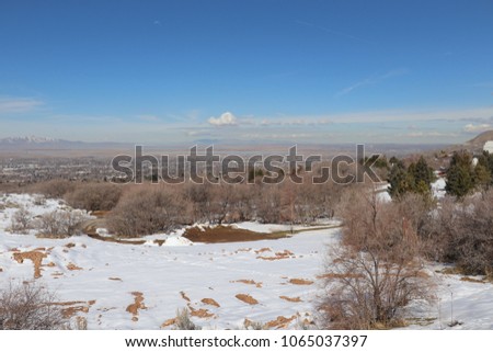 View of Farmington Bay from the hills in Bountiful Utah with snow, trees, blue sky with clouds, mountains and Bountiful city below
 