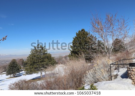 Lookout over a cemetery with budding trees, snow, sagebrush and bushes, pine trees and blue sky, above Farminton bay in Utah 