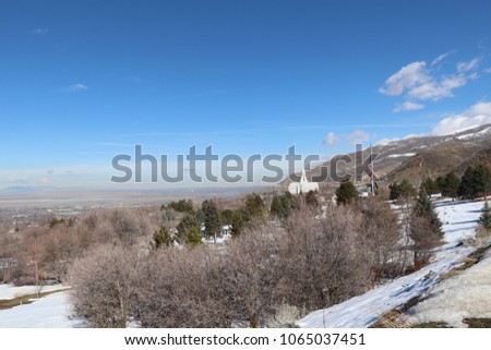 The Bountiful Utah mormon LDS temple with snow, bushes, pine trees, blue sky with white clouds, an American flag, and Farmington bay in the background