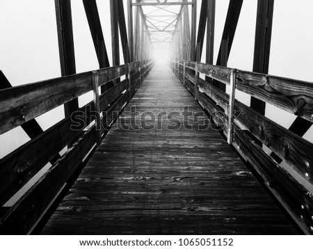 A stark black and white of an old truss footbridge over the lake on a foggy morning at Tims Ford State Park in Winchester Tennessee. Haunting or spooky yet mysterious ambiance.