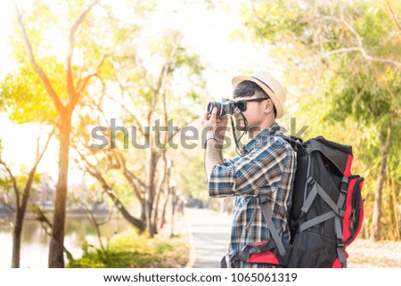 backpack young man traveler photographing holding digital camera on the road in the forest.