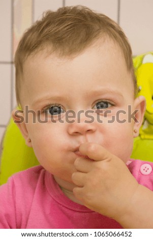 Happy cute baby in a pink blouse sitting in a high child's chair green color and eating food in the kitchen, closeup portrait