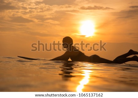 Surfer girl waiting in the line up for a wave at sunrise or sunset