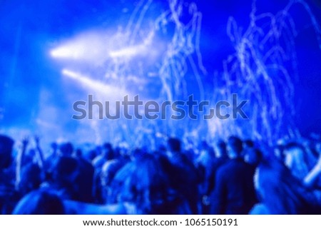 Blurred background with crowd of people partying and stage lights at a live concert