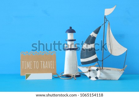 nautical concept image with sail boat, lighthouse and note over blue wooden table and background