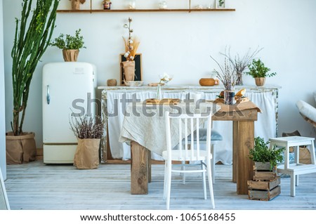 Beautiful spring photo of kitchen interior in light textured colors. Kitchen, living room with beige sofa sofa, old retro white fridge, rustic table, large cactus and woven macrame on the wall Royalty-Free Stock Photo #1065168455