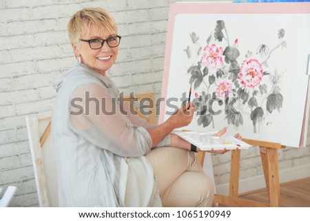 Portrait of happy creative senior woman painting on canvas