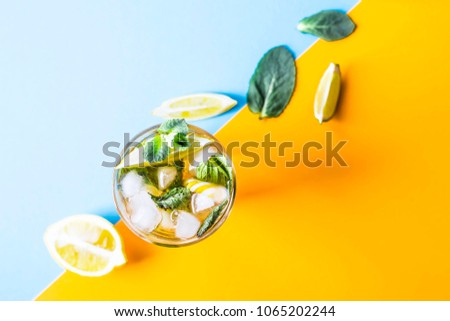 Ice tea with ice, lemon and mint on a combined colored yellow and blue background. Summer cold drink cocktail. Top view, flat lay Royalty-Free Stock Photo #1065202244