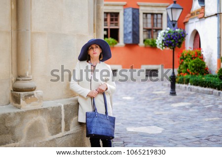Attractive modern woman standing on the city street.Fashionable young woman walking in street in the city wearing shirt hat and jacket. Fashion summer photo,old city.