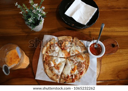 A pizza menu on a wooden table with chilli sauce plus a cold tea drink