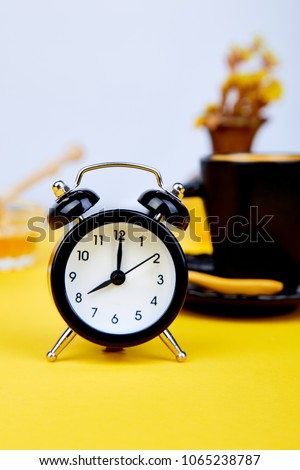 Morning coffee, granola breakfast with fruit near black alarm clock, vase flower on yellow background. Flat lay. Copy space. Top view.