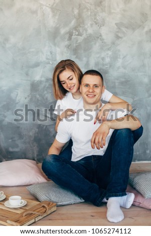 Young loving couple in white t-shirts embraces  sitting on the  floor. Copy space. Grey Background