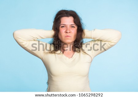 Young woman covering her ears over blue background
