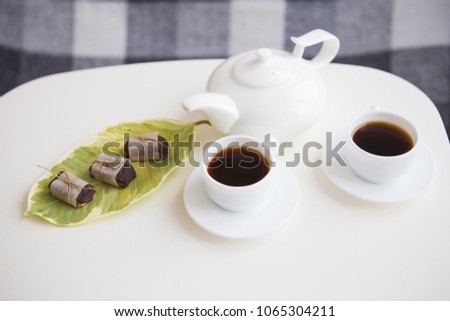 Two cups of coffee with a teapot stand on a table, candy made from nuts.