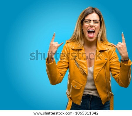 Beautiful young woman making rock symbol with hands, shouting and celebrating, blue background