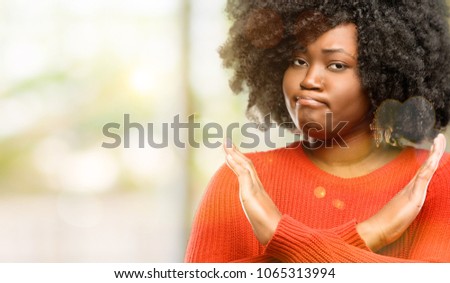 Beautiful african woman annoyed with bad attitude making stop sign crossing hands, saying no, expressing security, defense or restriction, outdoor