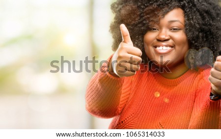 Beautiful african woman stand happy and positive with thumbs up approving with a big smile expressing okay gesture, outdoor