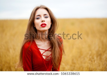 Portrait of a young brunette woman in red dress on a background of golden oats field, summer outdoors