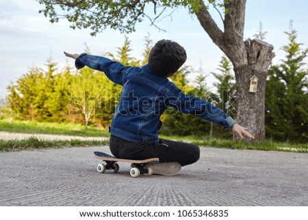 Kid skateboarder sitting on his skateboard and feels happy.