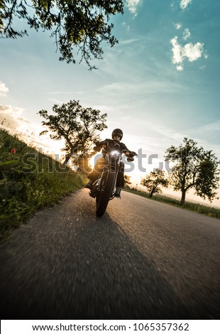Man riding sportster motorcycle on countryside during sunset. Royalty-Free Stock Photo #1065357362