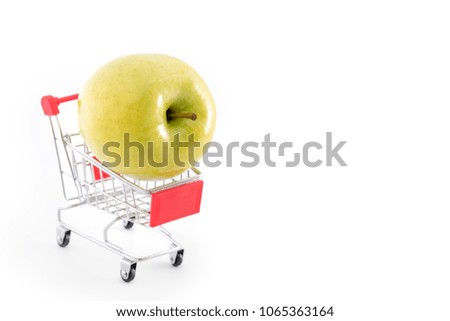 Shopping cart with big green apple on white. Buying fruits from supermarket. Self-service supermarket full shopping trolley cart. Sale, abundance, harvest theme. Copyspace for text.