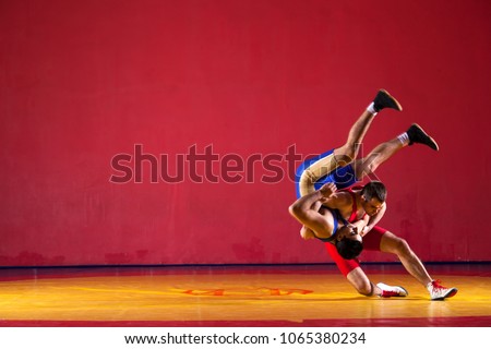 Two greco-roman  wrestlers in blue uniform wrestling   on a yellow wrestling carpet in the gym