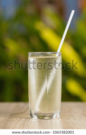 Transparent misted glasses with water and ice against a background of green bushes in different lighting
