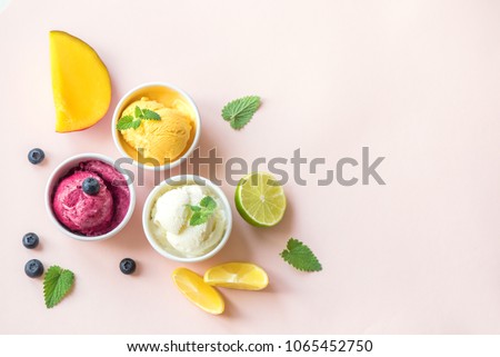 Three various fruit and berries ice creams on pink background, copy space. Frozen yogurt or ice cream with lemon, mango, blueberries - healthy summer dessert.